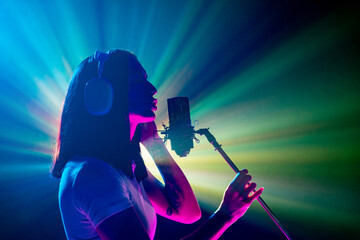 Side view portrait of performing artist, young brunette woman at microphone with radiant light show behind. Silhouette. Concept of art, work and hobby, music festivals, self expression, concert. Ad