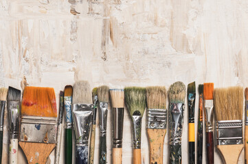 Row of old vintage paint brushes on a beige primed canvas background.Creativity concept.