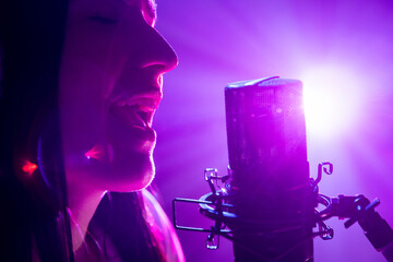 Close-up portrait of joyful singer's profile with microphone against purple backlight on stage with...
