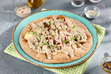 Whole wheat flatbread with vitello tonnato sauce and veal on a ceramic plate, olive oil, and condiments in the backdrop