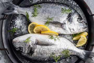 Raw fifh dorada with lemon slices, seasoning, and herb ready for cooking, directly above - 776111713