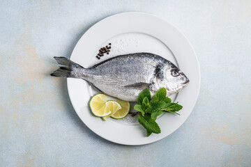 Raw fifh dorada with lime
slices, seasoning, and mint herb ready for cooking, directly above - 776111957