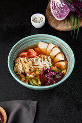 Chinese soup with noodles, chicken meat and vegetables in ceramic bowl on dark background. Asian cold soup in korean style and pick up noodles. Chinese cuisine in modern style..