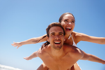 Couple, piggyback and freedom on beach with happiness for bonding, summer vacation and travel adventure. Man, woman and love by ocean with mockup space for getaway, healthy relationship and blue sky