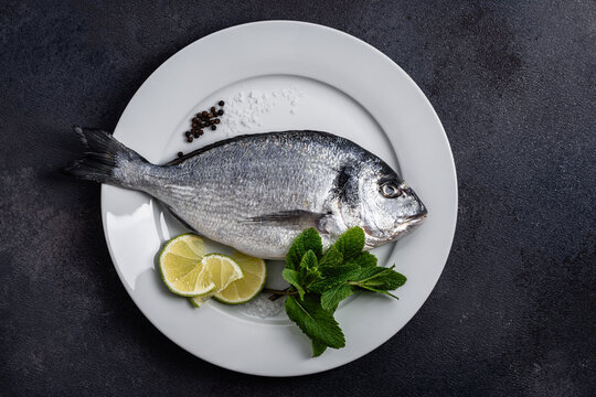 Raw fifh dorada with llime slices, seasoning, and mint herb ready for cooking, directly above