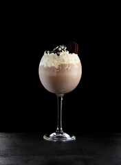 Chocolate milkshake in wine glass on black background. Milkshake with milk, ice cream and oreo cookie in minimal style. Oreo shake with ice cream and chocolate in glass.