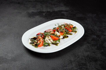 Traditional italian food - caprese salad with mozzarella cheese, tomatoes and pesto sauce. Caprese salad on black concrete background in minimal style. Italian appetizer caprese on dark background