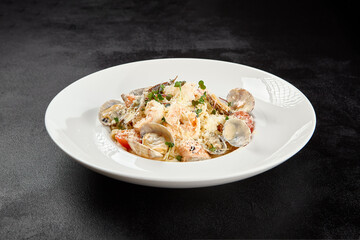 Seafood pasta with vongole, clams, salmon fish and prawns in white plate. Spaghetti marinara with seafood and cheese on dark background. Seafood menu -  pasta in mediterrian  style on black table.