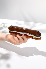 Female hand holding chocolate eclair. Woman take chocolate eclair. Hand with dessert. Trendy dessert menu. Coffee eclair with person.