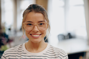 Portrait of young female manager in eyeglasses standing on office background and looks camera