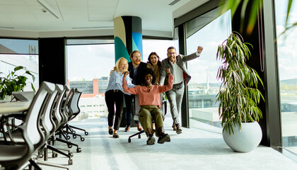 Joyful Office Colleagues Engage in a Playful Chair Race on a Sunny Afternoon.