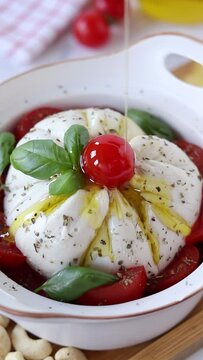 Olive oil pouring on vegan burrata cheese salad with cherry tomatoes and fresh basil. Vertical video. Close-up. Preparing healthy Italian food concept.