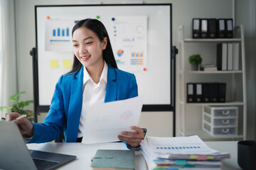 A woman in a blue suit is sitting at a desk with a white board behind her