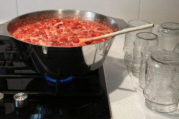 Cooking strawberry jam in a large bowl at home. Wooden spoon in a bowl with jam. Empty glass jars for jam.