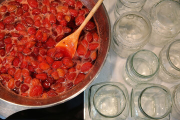 Cooking strawberry jam in a large bowl at home. Wooden spoon in a bowl with jam. Empty glass jars...