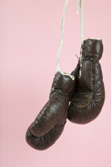 a pair of old boxing gloves hung in front of a candy-pink background