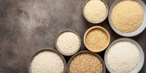 Collection of different types of dry rice in bowls on a on dark brown background. Top view, flat lay, copy space. Banner