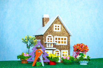 Brown house with keys on a Christmas tree and many flowers around on a light turquoise background