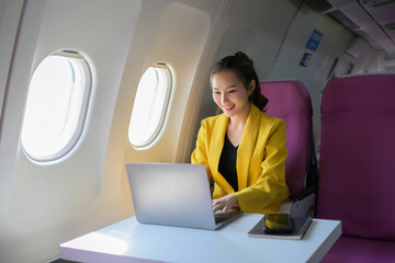 A woman is sitting in a plane and working on her laptop