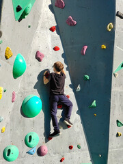 Fototapeta premium A teenage boy is exercising and climbing a rock-climbing wall. An example of the active sports life of young people