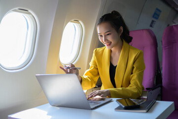 A woman in a yellow jacket is using a laptop computer on an airplane