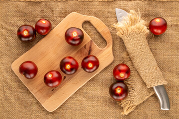 Several organic black cherry tomatoes with wooden kitchen board and knife on jute cloth, macro, top view.