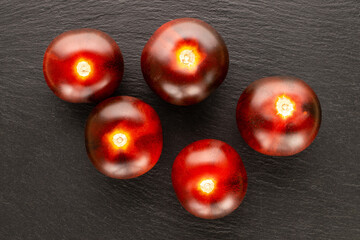 Several juicy black cocktail tomatoes on slate stone, macro, top view.