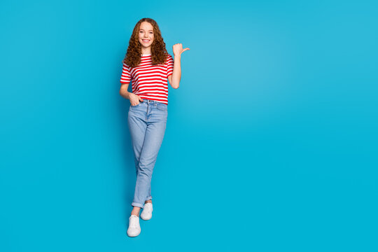 Full size photo of lovely cute girl wear stylish t-shirt denim trousers indicating at sale empty space isolated on blue color background