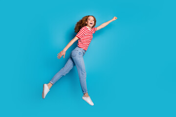Fototapeta na wymiar Full size photo of overjoyed girl wear stylish t-shirt pants jump stretching fist to empty space isolated on blue color background