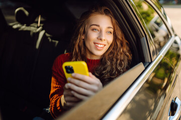 Happy woman using smartphone, sitting in the back seat of a car, scrolling social media news, reading email letters, communication with friends, messages, shopping online.