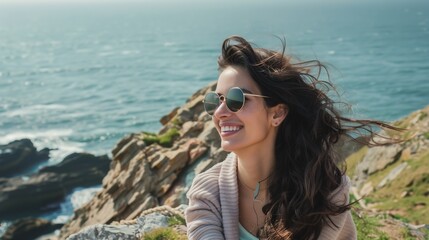 Fototapeta na wymiar A captivating portrait of a beautiful smiling brunette young natural woman wearing sunglasses, standing on a cliff overlooking a vast ocean