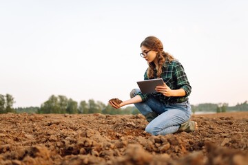 Farmer woman with a digital tablet holds black soil in her hands and checks the quality. Concept of technology, ecology and gardening.