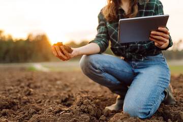 Farmer woman with a digital tablet holds black soil in her hands and checks the quality. Concept of...