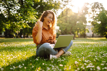 Young curly woman in the park with laptop on the green grass. Education online. IT. Business,...