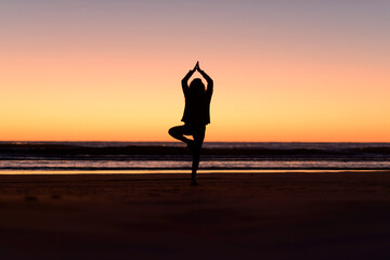Woman silhouette doing yoga postures at the beach before sunrise - obrazy, fototapety, plakaty
