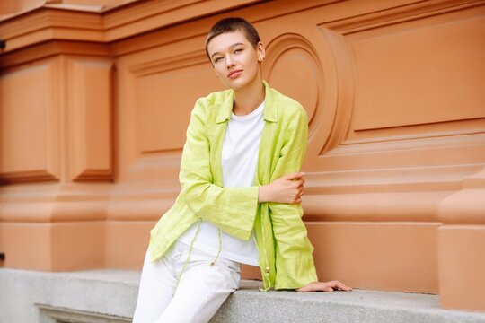 Positive young female in trendy outfit with short  hair smiling and looking at camera. Urban street fashion concept.