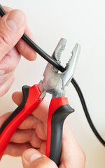 Close-up of hands using pliers to cut a black wire, highlighting a DIY electrical repair task.