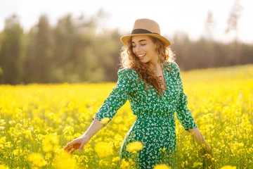Schilderijen op glas Beautiful woman walking in the field at sunny summer day. Nature, vacation, relax and lifestyle. View scenic landscape yellow flower blooming. © maxbelchenko