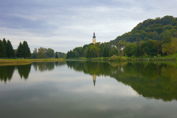 Fototapeta na wymiar View over the bathing lake to the Catholic parish church of St. Magdalena in Wildon, Austria.