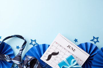 Dad’s day gala: An overhead display of Father's Day party decor with a June calendar, blue stars, striped necktie, mustache cutouts on blue background ready for festive messages