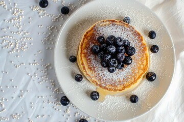 A plate of pancakes with blueberries and powdered sugar on top