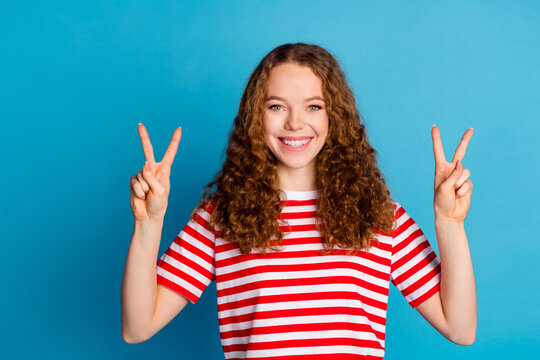 Portrait of optimistic adorable girl with curly hairdo wear stylish t-shirt showing v-sign symbol isolated on blue color background