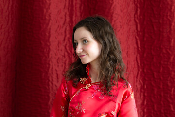 Horizontal half-profile portrait pretty brunette young woman in red satin asian top red background