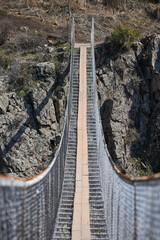 Suspension excursion bridge over gorge. Sightseeing holiday tour, Kyrgyzstan. Crossing between two mountains. Dangerous footbridge, frightening path fear of heights. Hiking trek, pathway, front view