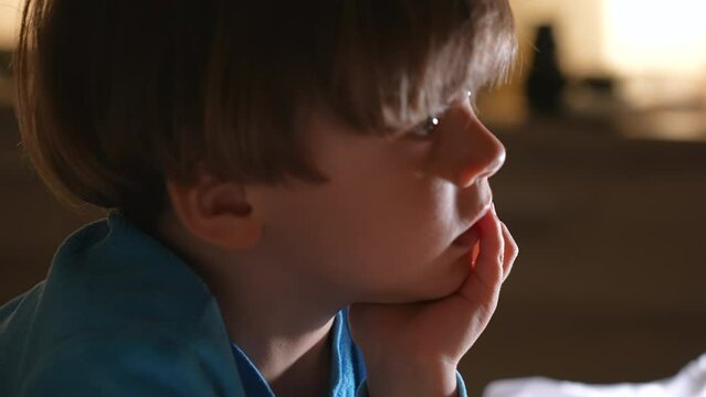 Close-up of pensive child with hand in chin in the evening. Portrait of small boy with thoughtful emotion
