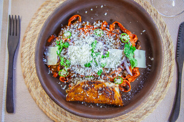 Pasta fresca hecha en casa teñida con puré de mix de chiles secos , con birria típica de Jalisco, acompañada de quesabirria, cebolla caramelizada, cilantro, chile serrano y queso nacional añejado