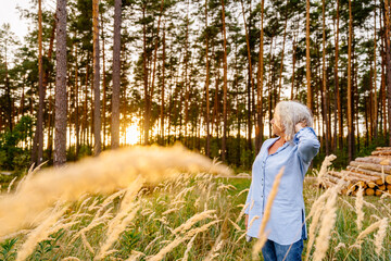 Active lifestyle in golden years concept. Side view shot of smiling positive senior woman with grey hair and enjoying the sunset at summer evening at beautiful nature woods.