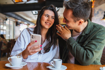 A young couple boyfriend and girlfriend or friends are drinking coffee having fun and taking selfies in cafe or restaurant 