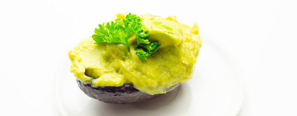 A green avocado with parsley on top sits on a white plate - 776207517