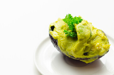 A green avocado with parsley on top sits on a white plate - 776207551